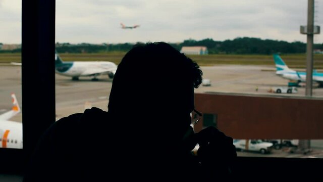 Silhouette of man drinking coffee and waiting at the airport for a flight while a airplane take off in the background