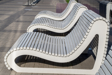A row of white designer benches consisting of sidewalls of streamlined rounded shape held together...