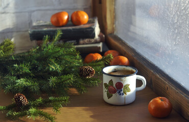 Hot coffee mug, tangerines, books, green spruce branches and winter wooden window
