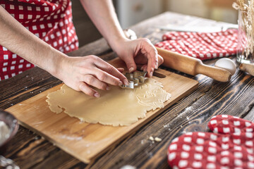 Woman making delicious homemade cookies in the shape of Christmas tree in her kitchen. Concept of fresh homemade cakes and cozy festive atmosphere