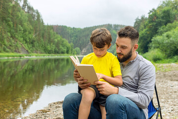 Fototapeta premium Father and son reading book while sitting outdoor on green natural background