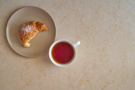 Tea break concept. Top view of teacup, fresh croissant on beige background. National Croissant Day.