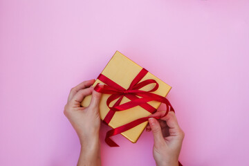 Gift box in the hands of a girl with a natural manicure on a pink background with a copy of the space. Unpacking a gift. Christmas, New year, birthday, Valentine's day greetings concept.