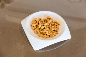Tasty cashew nuts in plate on wooden table. white plate with cashew nuts on wooden table. Roasted cashew nuts 