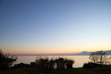View from the embankment on water of sea and pink and yellow sunset on horizon in background