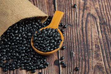 Fototapeta na wymiar black bean in small wooden spoon place next to sack bag full of black bean