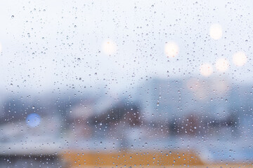 Window in the rain, large drops of rain on the glass, blurred outlines of the city in the background. Abstract texture