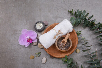 Rolled towels and salt spoon in bowl in wooden bowl, eucalyptus leaves,stone and,candle ,pink orchid on grey background