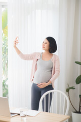 Fototapeta na wymiar A young pregnant woman standing next to the window taking a selfie