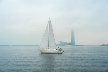 Fototapeta na wymiar Sailboat in the waters of the Gulf of Finland. Saint-Petersburg, Russia. Foggy cloudy day, blue sky with low clouds and blue water.