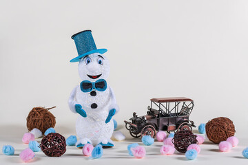 A cheerful snowman in a blue outfit stands surrounded by an old retro car and brown balls on a...