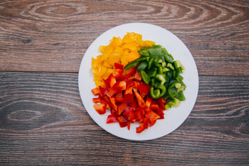 Diced multi-colored bell peppers on a white plate. On a dark wooden background. Red, yellow and green