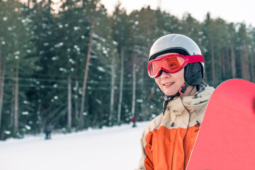 Portrait of a woman snowboarder wearing helmet and goggles in front of forest and slope