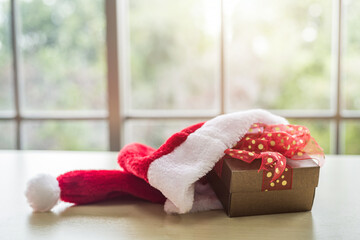 Santa Claus hat with Gift boxes placed on wooden table interior of room view through window with tree Background with Copy Space,Decoration During Christmas and New Year.