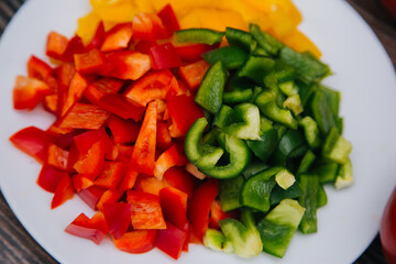 Diced multi-colored bell peppers on a white plate. On a dark wooden background. Red, yellow and...