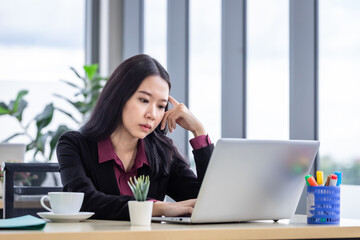 Upset thoughtful Young Asian business woman stress in the workplace working with laptop computer of Office staff are not happy in with working colleagues behind in the office