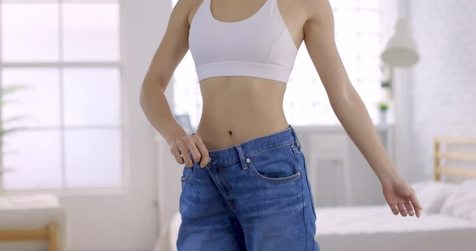 Young slim woman in  big jeans showing her diet results at home