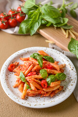 Plate of delicious penne pasta with tomato sauce on color background
