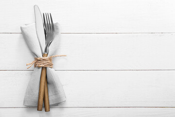 Cutlery and napkin on light wooden background