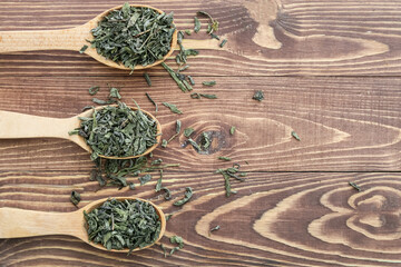 Spoons with dry green tea on wooden table