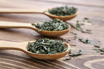 Spoons with dry green tea on wooden table
