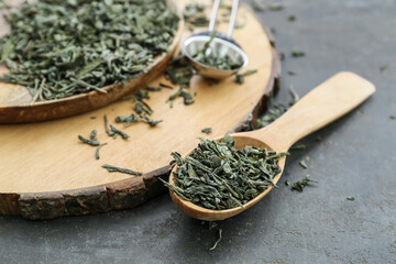 Spoons with dry green tea on dark table