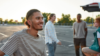A close up of a casually dressed dark-skinned latina guy with a piercing smiling standing outside...
