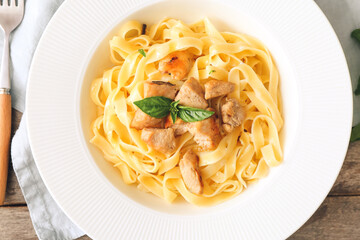 Plate of tasty pasta with chicken on wooden table