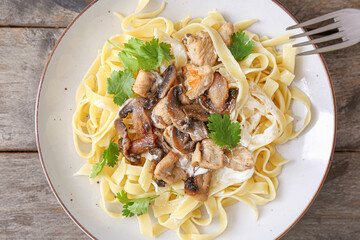 Plate of tasty pasta with chicken and mushrooms on wooden table