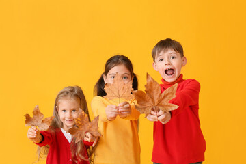 Cute little children with autumn leaves on color background