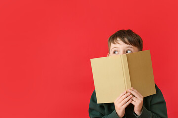 Cute little boy in autumn clothes and with book on color background