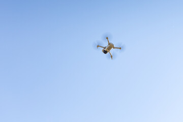 White unmanned aerial vehicle with four propellers and blades is in the blue sky background