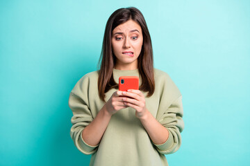 Photo portrait of girl biting lower lip holding phone in two hands isolated on vivid turquoise colored background