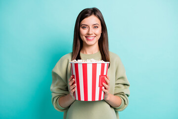 Photo portrait of cheerful girl holding huge popcorn bucket with two hands isolated on vivid teal...