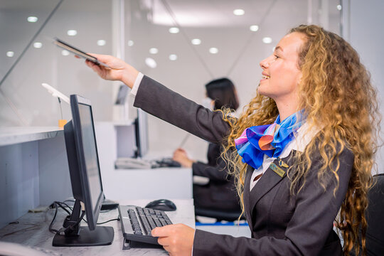 Gorgeous Caucasian Airline Ground Staff Receiving A Passport From The Passenger To Check And Print Out A Boarding Pass At The Airport. During A Covid-19 Pandemic Around The World.