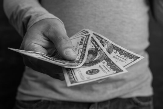 Men's hands hold one hundred dollar bills. Black and white photo