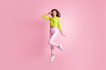 Full length photo of cute girl jump show v-sign wear green sweater pants footwear isolated pink...