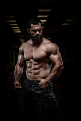 Fototapeta na wymiar strong young bearded athlete male with perfect sport physique body torso muscle in dark fitness gym