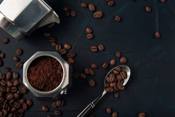 Metal spoon with coffee beans and coffee maker on dark textured background. Top view. Copy space.