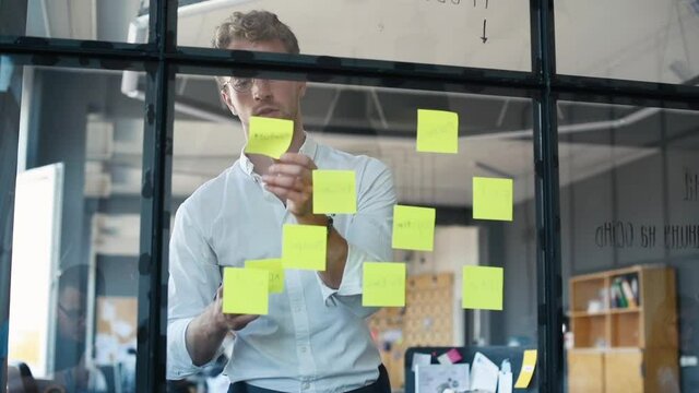 Young business people in formal clothes planning work in the office with paper stickers on the glass.