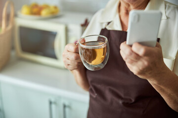 Elderly woman holding cup of tea and mobile phone