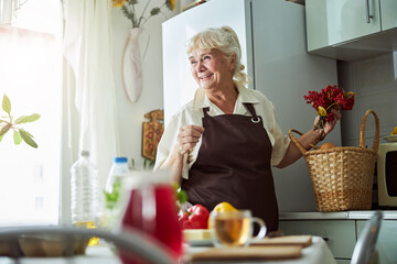 Cheerful old woman in apron standing in kitchen