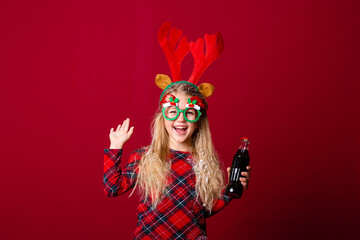 a little girl in Christmas glasses holding a bottle with a drink. Christmas concept, red background, text space