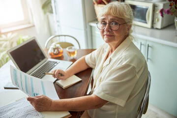 Lovely old woman filling out taxes form at home - Powered by Adobe
