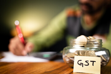 selective focus on coins in bottle and GST sticky note, man in background checking spending's on...