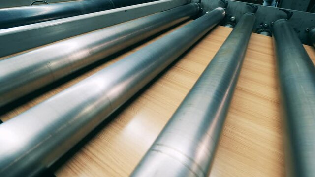 Closeup of sheet metal with wood grain coating moving through rolling mill