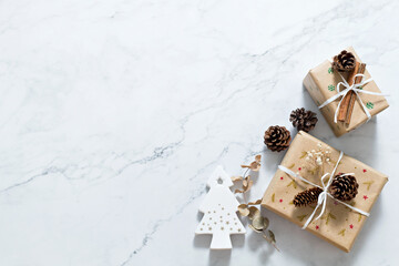 Christmas composition on white marble background with white christmas tree, gift box, gold ribbon and pine cone. Minimal, flat lay with copy space.