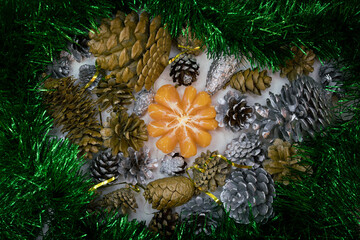 Peeled fresh bright mandarin amidst green and shimmering tinsel with cones painted in silver and gold.