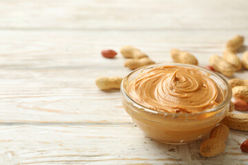 Peanut and bowl with peanut butter on wooden background