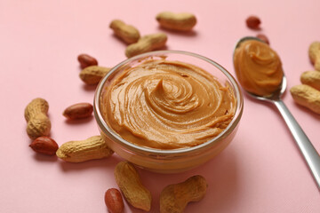 Peanut, bowl and spoon with peanut butter on pink background